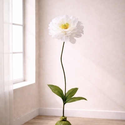 Flor artificial branca com folha e base verde num chão de madeira junto a parede e janela