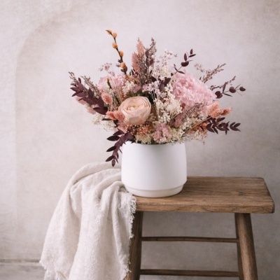 Arranjo floral com flores rosa, vaso branco e banco de madeira