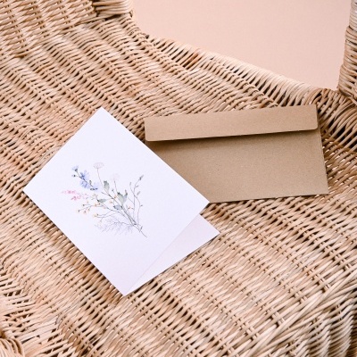 Cartão floral e envelope de papel castanho sobre cadeira de vime