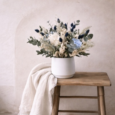 Jarro branco com arranjo de flores secas sobre banca de madeira e tecido branco