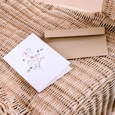 Cartão branco floral com envelope castanho em cadeira de verga