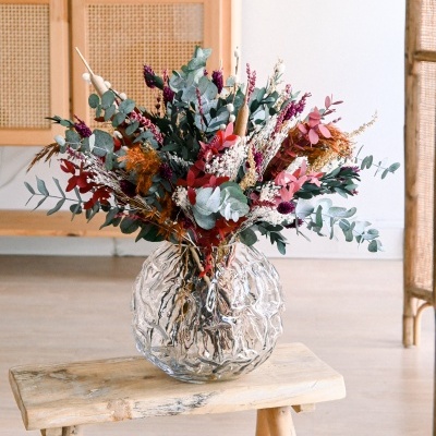 Vaso redondo de vidro com flores secas coloridas sobre banco de madeira