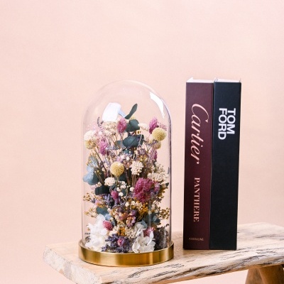 Arranjo de flores em cúpula de vidro ao lado de caixas de perfumes sobre banco de madeira