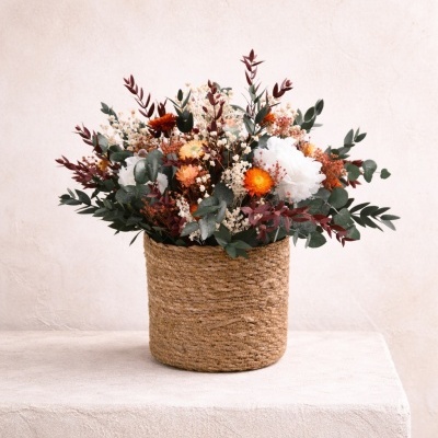 Arranjo floral em vaso de palha com flores secas e frescas coloridas sobre superfície clara