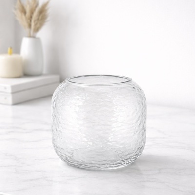 Jarro de vidro transparente com textura martelada sobre mesa branca de mármore