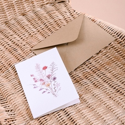 Cartão com ilustração floral e envelope castanho sobre cadeira de vime