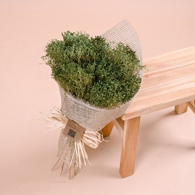 Bouquet de flores verdes embaladas em rede bege ao lado de banco de madeira clara