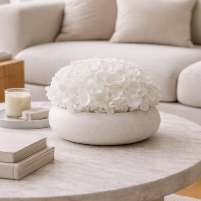 Arranjo de flores brancas em vaso cerâmico creme numa mesa de centro clara