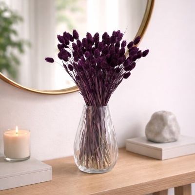 Vaso de vidro com flores secas roxas em consola de madeira com vela e pedra, espelho dourado ao fundo