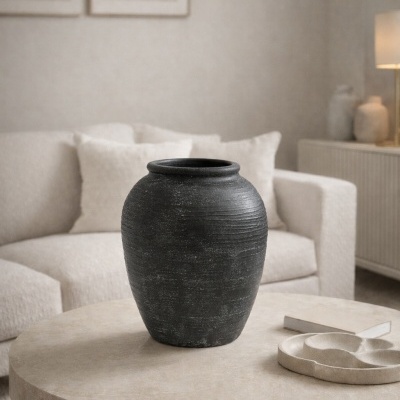 Jarro preto de cerâmica na mesa redonda beige em sala com sofá creme e almofadas.
