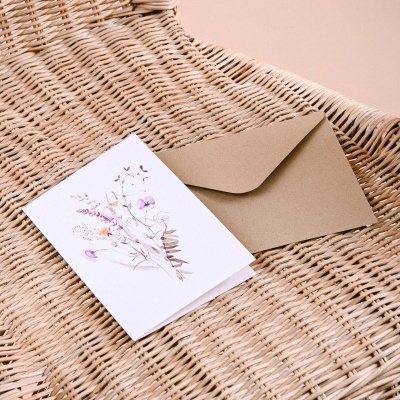 Cartão com ilustração de flores e envelope castanho sobre cadeira de rattan
