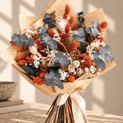 Ramo de flores secas laranja, brancas e verdes acinzentadas com papel castanho e fita branca