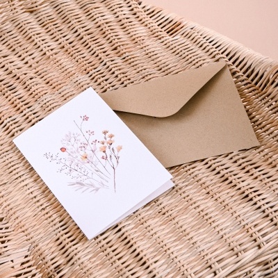 Cartão com flores secas e envelope castanho numa cadeira de vime clara