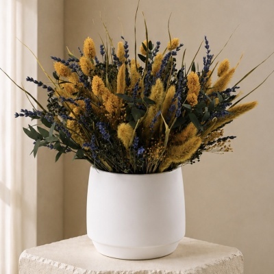 Arranjo de flores secas amarelas e violetas em vaso branco sobre pedestal de pedra