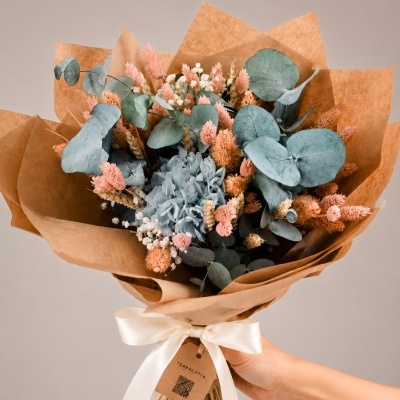 Bouquet de flores secas e preservadas em papel castanho claro com fita branca e etiqueta terracotta.