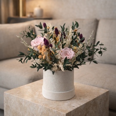 Arranjo floral em base cilíndrica bege sobre mesa de pedra clara