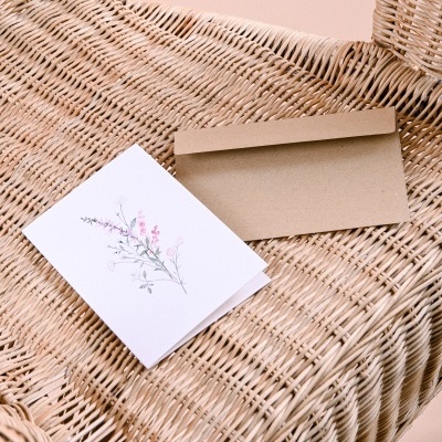 Cartão floral branco e envelope castanho sobre cadeira de vime