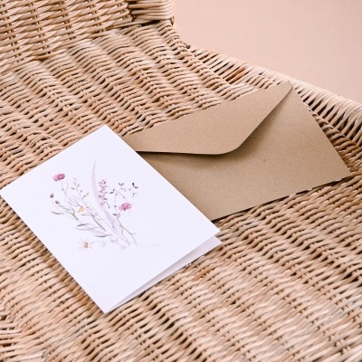 Cartão de felicitações florido e envelope castanho sobre cadeira de vime