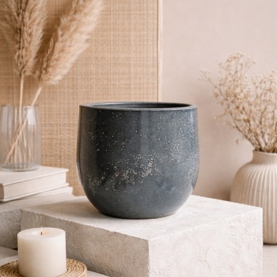 Vaso de cerâmica preta com textura e manchas brancas em decoração com vela branca, plantas secas e livros.