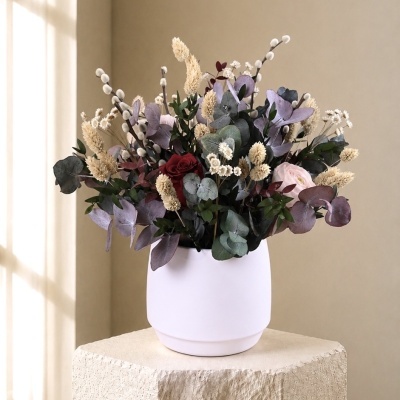 Arranjo de flores secas e preservadas num vaso branco fosco