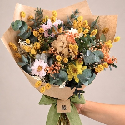 Buquê de flores secas coloridas envolto em papel kraft com fita verde