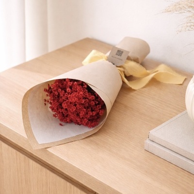 Buquê de flores secas vermelhas em papel pardo com fita amarela numa mesa de madeira.