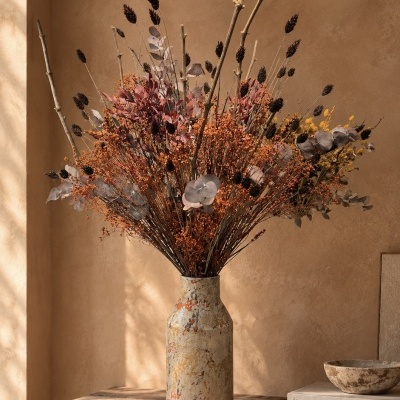 Vaso de cerâmica com flores secas coloridas em mesa de madeira rústica