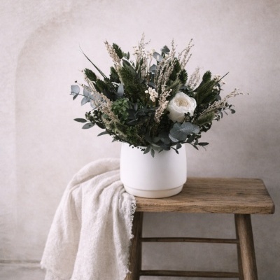 Arranjo floral em vaso branco sobre mesa de madeira com tecido branco