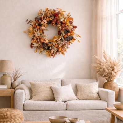 Sala de estar com sofá bege, almofadas, mesa de madeira, coroa floral seca outonal pendurada na parede.