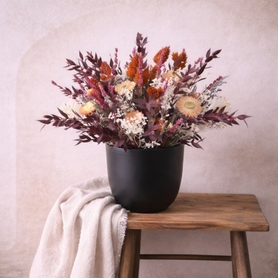 Vaso preto com flores secas coloridas sobre banco de madeira com tecido