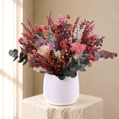 Arranjo de flores secas em vaso branco sobre pedestal de pedra