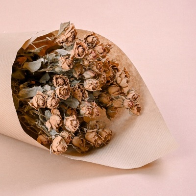 Ramo de flores secas em papel castanho claro sobre fundo rosa