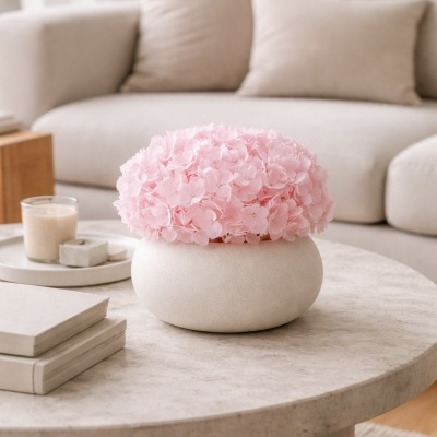 vaso branco redondo com flores cor-de-rosa em mesa de mármore em sala com sofá bege