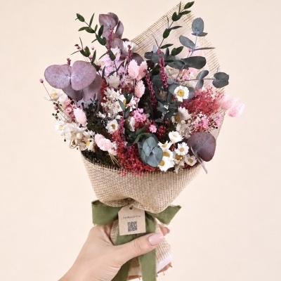 Buquê de flores secas em papel juta com fita verde nas mãos.