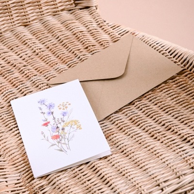 Cartão de flores com envelope castanho sobre cadeira de verga