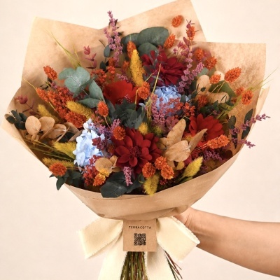 Bouquet de flores secas e naturais coloridas embrulhado em papel castanho com laço creme.