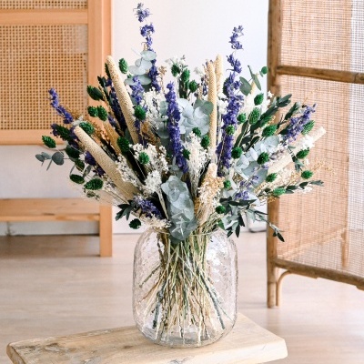 Arranjo floral com flores secas em vaso de vidro sobre banco de madeira em ambiente com móveis em rattan