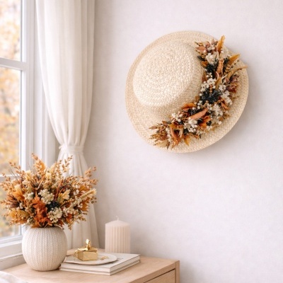 Chapéu de palha decorado com flores secas pendurado na parede ao lado de uma mesa com vaso de flores e vela