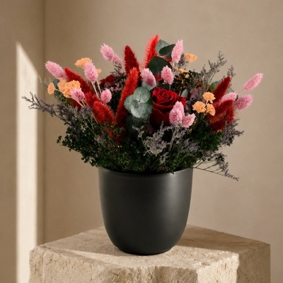 Arranjo floral com flores vermelhas, cor-de-rosa, laranja e roxas num vaso preto fosco.