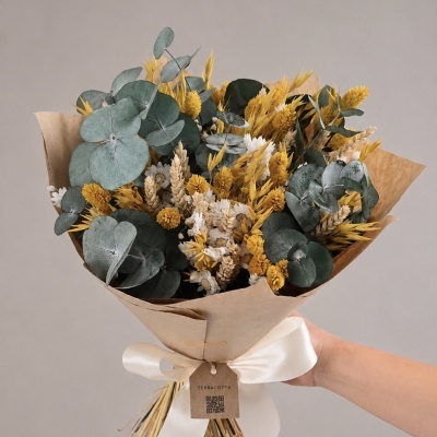 Ramo de flores secas com folhas verdes e flores amarelas e brancas envolto em papel castanho e fita branca