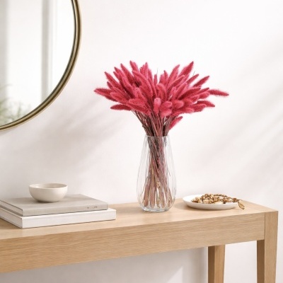 Aparador decorado com flores cor-de-rosa num vaso de vidro, livros, taça cerâmica, prato com contas de madeira e espelho redondo dourado