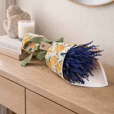 Buquê de flores secas roxas em papel floral com fita verde numa cómoda de madeira clara