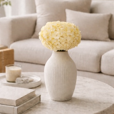 Vaso branco com flores amarelas numa mesa redonda de mármore numa sala moderna com sofá cinza ao fundo