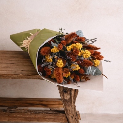 Bouquet de flores secas coloridas embrulhado em papel verde e branco sobre mesa de madeira.