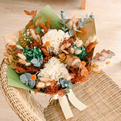 Bouquet de flores secas e preservadas com decoração em papel, sobre cadeira de vime
