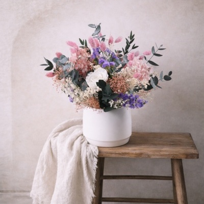 Arranjo floral variado em vaso branco sobre banco de madeira com tecido branco