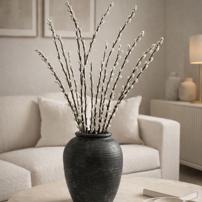 Vaso preto de cerâmica com raminhos decorativos brancos numa mesa redonda em sala clara.