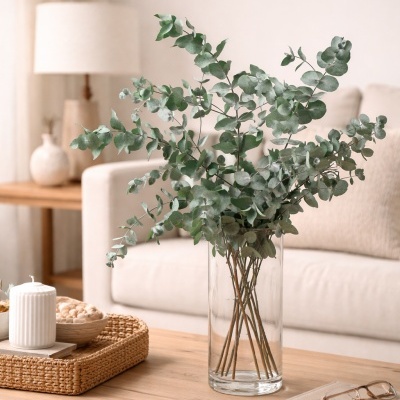 Vaso de vidro com folhas verdes em mesa de madeira com vela, bowl e livros