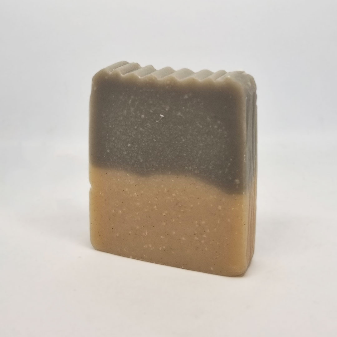 Sabonete de Vetiver e Argila Negra Sabonete artesanal cinzento e bege com topo ondulado sobre fundo branco