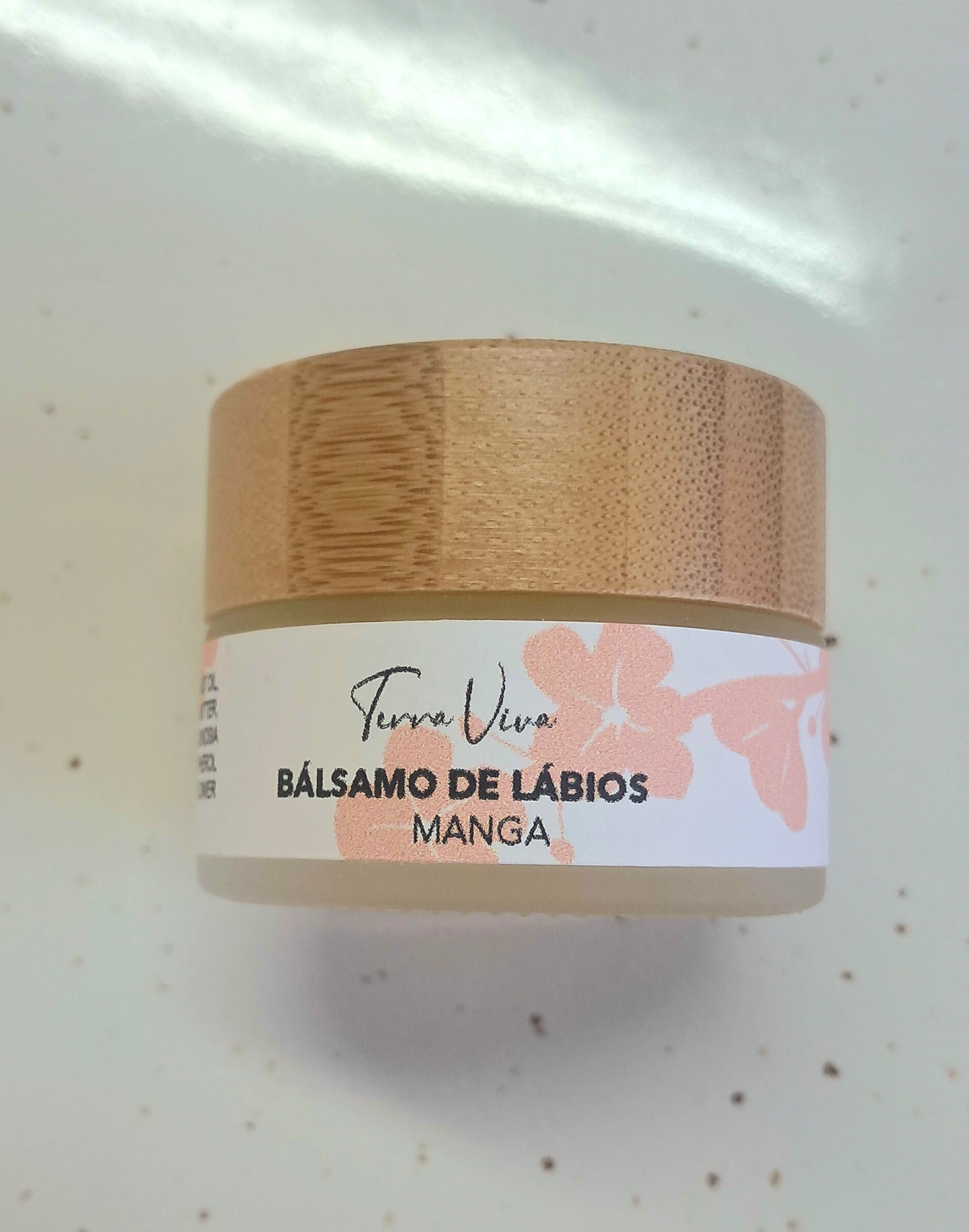 Bálsamo de Lábios 15gr Frasco de bálsamo de lábios com tampa de madeira clara e rótulo branco com flores cor-de-rosa.
